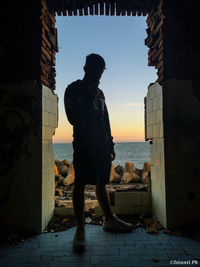 Silhouette man standing by sea against sky during sunset