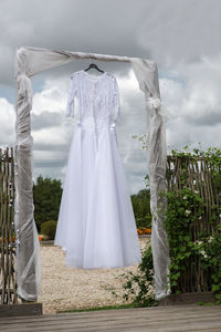 Bride dress hanging on wood against cloudy sky