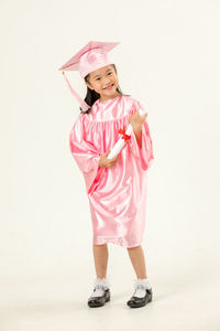 Full length of girl in pink graduation gown against white background