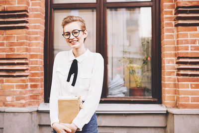 Portrait of smiling young woman standing against brick wall