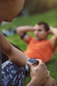 Woman touching smart watch while man doing sit ups at park