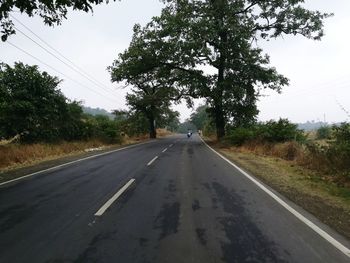 Road by trees against sky