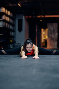 Full body young sporty female in fitness outfit performing stretching exercise on the floor while warming up during training in gym