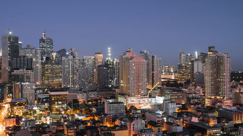 Illuminated modern buildings in city against clear sky