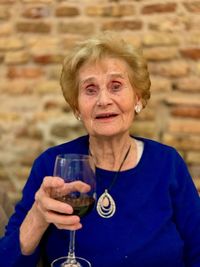Portrait of senior woman having drink in wineglass against brick wall