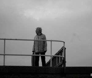 Woman standing by railing against sky