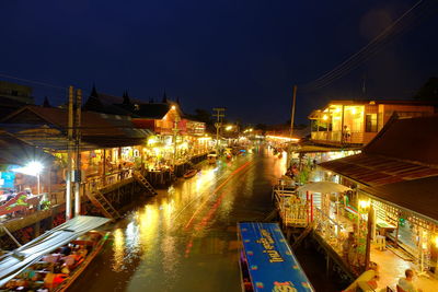 Boats on canal at illuminated floating market in city during night