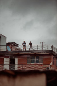 Low angle view of people standing on railing against sky