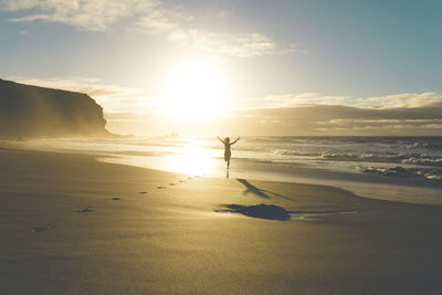 Woman at the beach running to the water at sunset