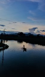 Silhouette man in lake against sky during sunset