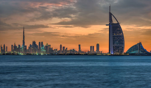 Sea and buildings in city at sunset