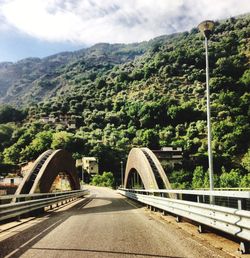 Bridge over road by trees against sky