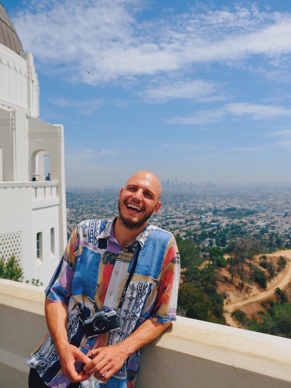 PORTRAIT OF SMILING MAN STANDING ON CITY AGAINST MOUNTAIN