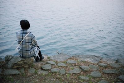 Rear view of woman sitting on rock by sea