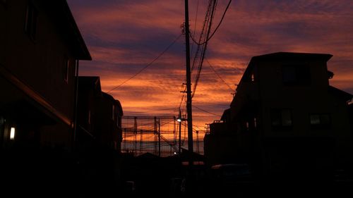 Low angle view of electricity poles amidst silhouette buildings against orange sky