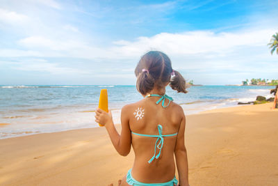 Rear view of girl with flower made with suntan lotion at beach