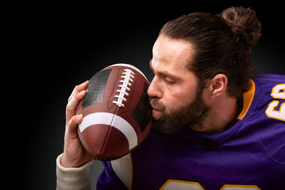 Portrait of man holding ball against black background