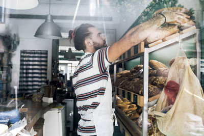 Young male entrepreneur arranging food seen through glass of bakery