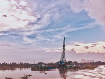 Cranes in city against sky during sunset