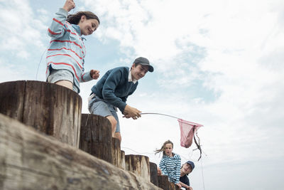 Happy friends catching crab while standing on wooden railing against cloudy sky