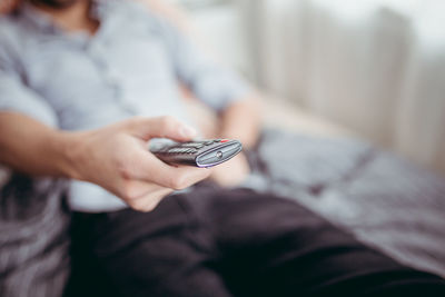 Midsection of man holding remote control at home