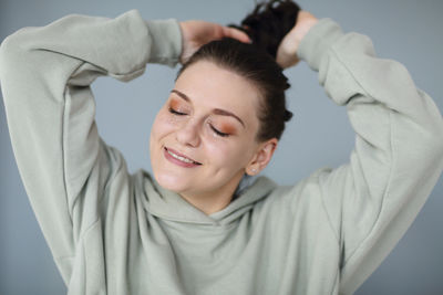 Young woman tying hair against colored background