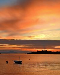 Silhouette boat in sea against dramatic sky during sunset