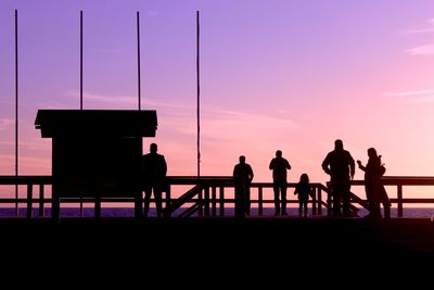 Silhouette people standing by railing against sky during sunset