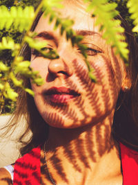 Close-up of woman with eyes closed and shadow of leaves on face