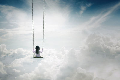 Digital composite inage of girl swinging against cloudy sky