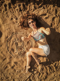 Full length of woman lying by bitcoin symbol at beach