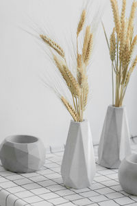 Stylish high gray concrete multi-faceted vases with bouquet dried flowers and spikelets, monochrome