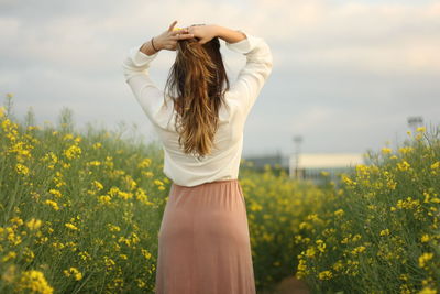 Rear view of woman tying hair while standing amidst plants