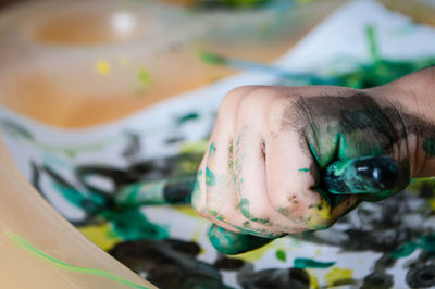 Cropped hand of child holding paintbrush on paper