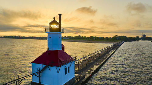 Lighthouse by sea against sky during sunset
