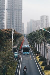 Man riding motor scooter on road amidst trees against buildings