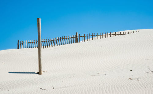 Wooden posts on beach against clear blue sky