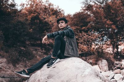 Portrait of young man sitting on rock against trees