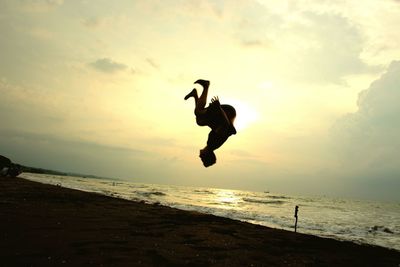 People jumping on beach against sky during sunset