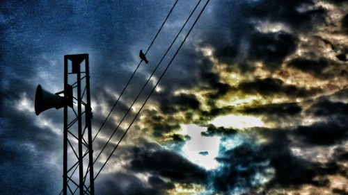 Low angle view of electricity pylon against cloudy sky