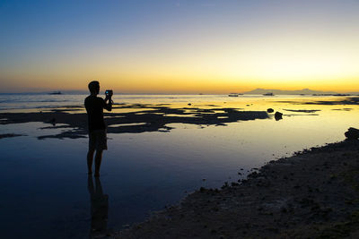 Silhouette of man standing on beach at sunset