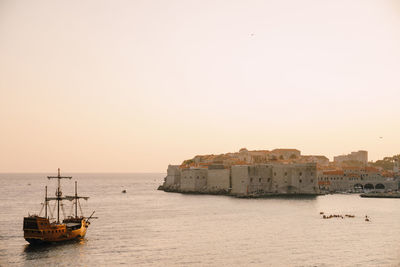 Sailboats on sea by buildings against clear sky during sunset