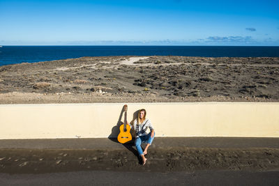 Full length of young woman with guitar sitting at beach