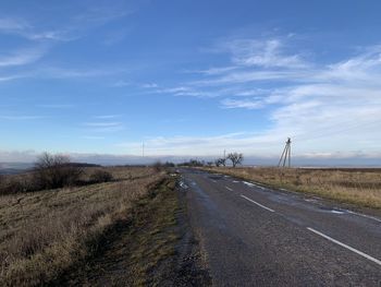 Empty road amidst field against sky