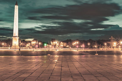 Illuminated footpath by street against sky at night