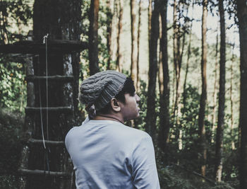 Side view of young man standing against trees in forest