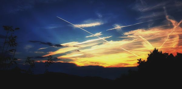 Low angle view of vapor trails in sky at sunset