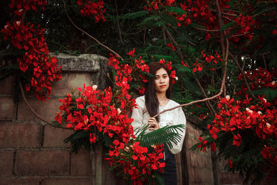 Woman standing by red flowering plants