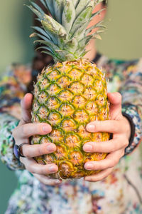 Midsection of woman holding pineapple against green background