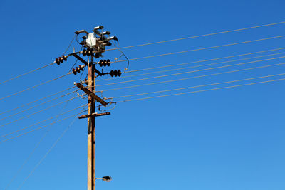 Low angle view of electricity pylon against clear blue sky